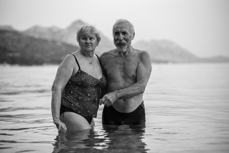 Elderly couple swims in the sea. Old bearded man and aged woman in swimsuits together stand in the tranqise water of the Adriatic sea at sunset.の写真素材