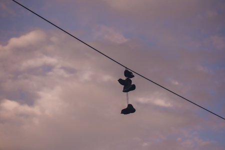 Old garland sneakers hang on an electric wire against the sky and clouds. Modern teenagers culture.の写真素材