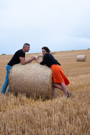 A young couple of beautiful people have fun in the field near round bales of dry hay. A man in a...