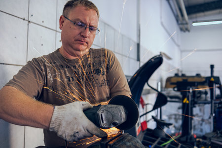 A man works as a grinder in a workshop. A master in glasses grinds a part clamped in a vice with a...