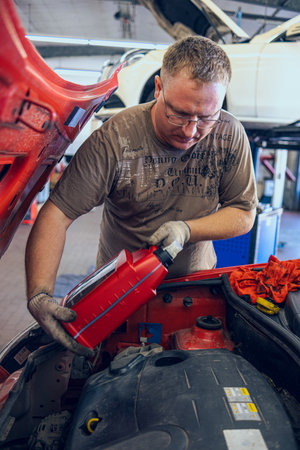 A Man with glasses Maintains a Car in a Garage. Car Repair by an experienced Specialist in a Car Repair Shop. Replacing the oil and filter in the car. An auto mechanic performs car repairs.の写真素材
