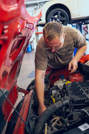 A Man with glasses Maintains a Car in a Garage. Car Repair by an experienced Specialist in a Car Repair Shop. Replacing the oil and filter in the car. An auto mechanic performs car repairs.の写真素材