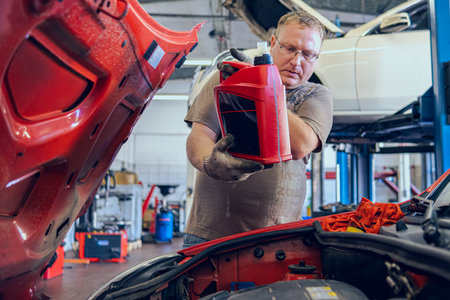 A Man with glasses Maintains a Car in a Garage. Car Repair by an experienced Specialist in a Car Repair Shop. Replacing the oil and filter in the car. An auto mechanic performs car repairs.の写真素材