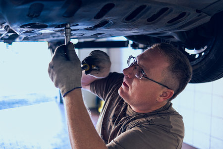 A Man with glasses Maintains a Car in a Garage. Car Repair by an experienced Specialist in a Car Repair Shop. Replacing the oil and filter in the car. An auto mechanic performs car repairs.の写真素材