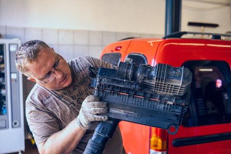 A Man with glasses Maintains a Car in a Garage. Car Repair by an experienced Specialist in a Car Repair Shop. Replacing the oil and filter in the car. An auto mechanic performs car repairs.の写真素材