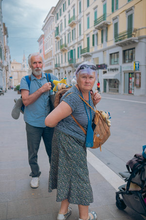 An elderly couple is traveling around Europe. Grandfather and grandmother with backpacks walk around the city in Italy. Old people enjoy traveling.の写真素材