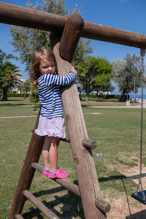 A little cute girl walks on the playground on a sunny summer day. The girl rides on a slide, a bungee, and climbs a slide.の写真素材