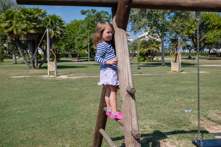 A little cute girl walks on the playground on a sunny summer day. The girl rides on a slide, a bungee, and climbs a slide.の写真素材