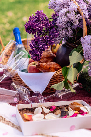Still life with a basket of lilac flowers, glasses, wine, fruit and croissants. Beautiful picnic close-up picture.の写真素材