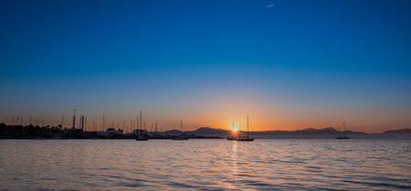 Sea harbor at dawn. The sky, painted golden by the rising sun, is reflected in the calm ripples of the sea. The yachts stand out in beautiful silhouettes against the sky, bathed in the light of dawn.の写真素材