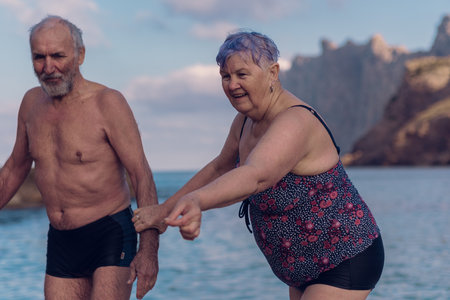 Old people swim in the sea. An elderly couple enjoys life by spending time at sea. An old grandfather and grandmother in a swimsuit are walking along the sea.の写真素材