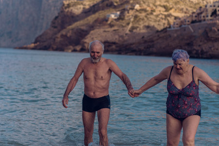 Old people swim in the sea. An elderly couple enjoys life by spending time at sea. An old grandfather and grandmother in a swimsuit are walking along the sea.の写真素材