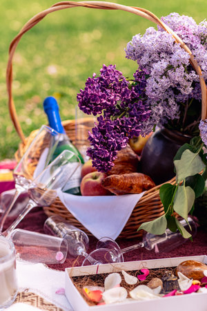Still life with a basket of lilac flowers, glasses, wine, fruit and croissants. Beautiful picnic close-up picture.の写真素材