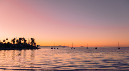 Sea harbor at dawn. The sky, painted golden by the rising sun, is reflected in the calm ripples of the sea. The yachts stand out in beautiful silhouettes against the sky, bathed in the light of dawn.の写真素材