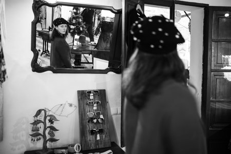 Photography in vintage style in black and white. A young girl tries on a hat in a store. Inside the boutique there is a characteristic atmosphere - a lot of clothes and accessories.の写真素材