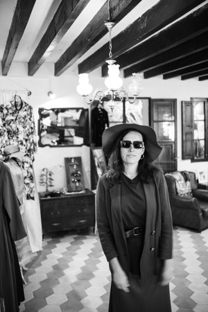 Photography in vintage style in black and white. A young girl tries on a hat in a store. Inside the boutique there is a characteristic atmosphere - a lot of clothes and accessories.の写真素材