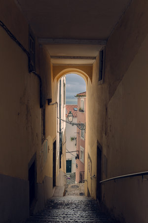 View of the sea and sky through a narrow dark arch with steps. Lisbon, old city, tiled roofs and a beautiful view of the sea through a narrow arch.の写真素材