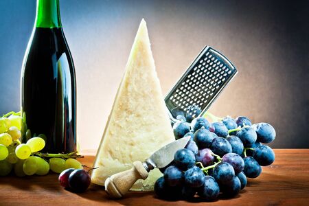 table with grapes, bottle of wine, cheese and grated.の写真素材