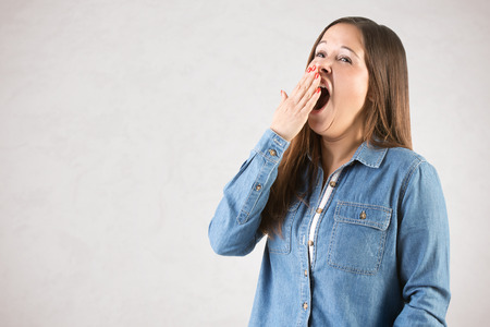 Pretty sleepy woman yawning, isolated in greyの写真素材