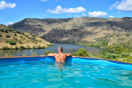Man relaxing in a swimming pool looking and the Douro Valley landscapeの写真素材