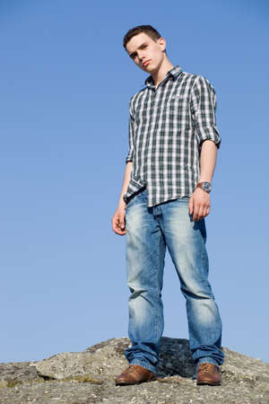 young casual man on top of a rock with the sky as backgroundの写真素材