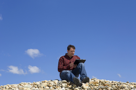 Young casual man working with touch pad at the beachの写真素材