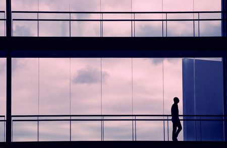 Silhouette view of young businessman walking in modern office building interior with panoramic windows.の写真素材
