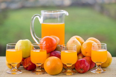 glasses of orange juice and lots of fruits on wooden table outdoorの写真素材
