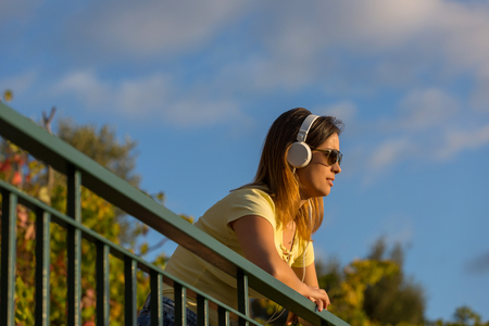 beautiful casual woman enjoying music at the sunset, with headphones, outdoorの写真素材