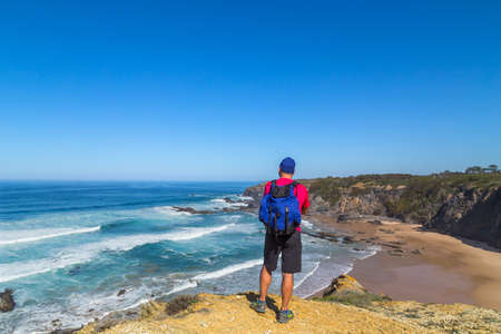 traveler with a backpack admires the beautiful view of the Atlantic Ocean and the coast of Alentejo in Portugalの写真素材