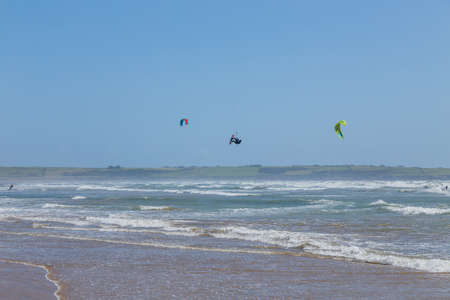 Ireland beach view with kitesurfing athletes. Kitesurfers rush at high speed across the surface of the sea for kites flying in the cloudless sky. Summer sunny day.のeditorial素材