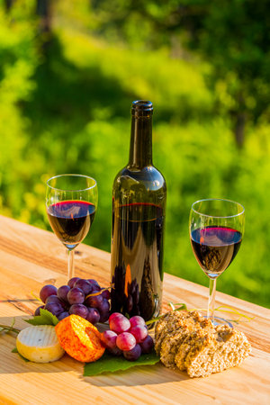 wine bottle, grapes, cheese and bread, on wooden table, outdoorの写真素材