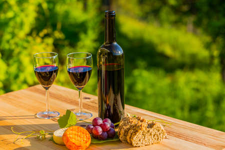 wine bottle, grapes, cheese and bread, on wooden table, outdoorの写真素材