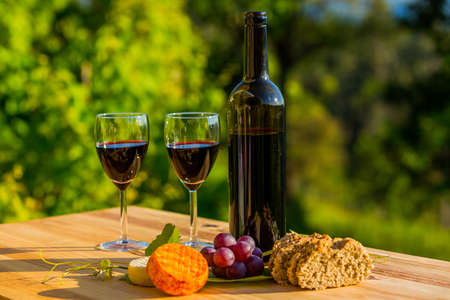 wine bottle, grapes, cheese and bread, on wooden table, outdoorの写真素材