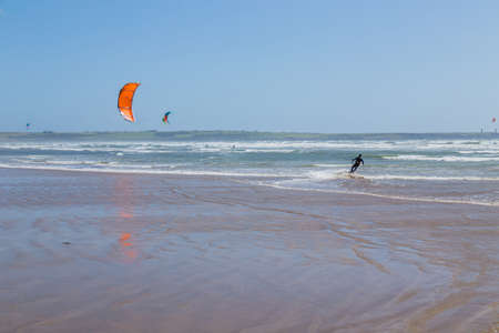 Ireland beach view with kitesurfing athletes. Kitesurfers rush at high speed across the surface of the sea for kites flying in the cloudless sky. Summer sunny day.のeditorial素材