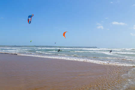 Ireland beach view with kitesurfing athletes. Kitesurfers rush at high speed across the surface of the sea for kites flying in the cloudless sky. Summer sunny day.のeditorial素材