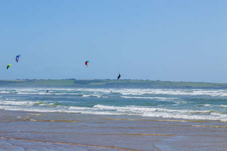 Ireland beach view with kitesurfing athletes. Kitesurfers rush at high speed across the surface of the sea for kites flying in the cloudless sky. Summer sunny day.のeditorial素材