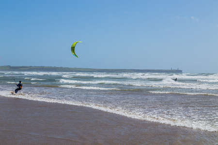 Ireland beach view with kitesurfing athletes. Kitesurfers rush at high speed across the surface of the sea for kites flying in the cloudless sky. Summer sunny day.のeditorial素材