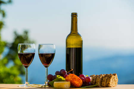 wine bottle, grapes, cheese and bread, on wooden table, outdoorの写真素材