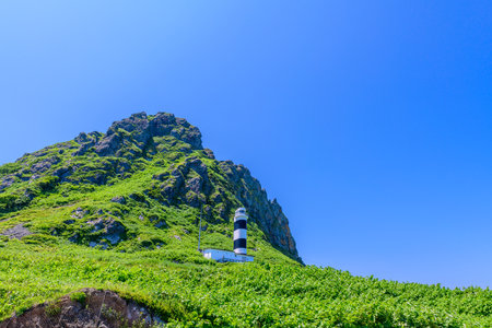 A tranquil summer view of Cape Kamui in Kitami, Hokkaido, Japan. The scene is filled with deep blue skies and vast ocean under brilliant sunlight, capturing the peaceful atmosphereの写真素材