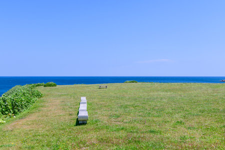 A tranquil summer view of Cape Kamui in Kitami, Hokkaido, Japan. The scene is filled with deep blue skies and vast ocean under brilliant sunlight, capturing the peaceful atmosphereの写真素材