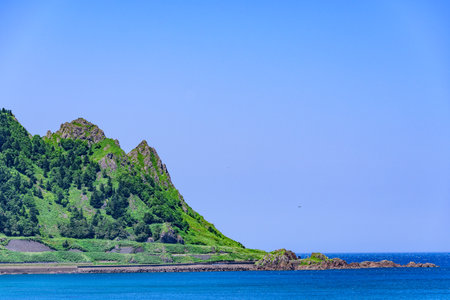 A tranquil summer view of Cape Kamui in Kitami, Hokkaido, Japan. The scene is filled with deep blue skies and vast ocean under brilliant sunlight, capturing the peaceful atmosphereの写真素材