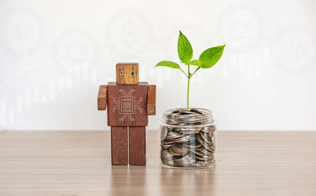 Saving and Investment concept by using Artificial intelligence procession. A green plant growing on  a jar of coins with the wooden robot and business graphs background.の写真素材