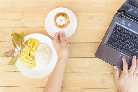 Mango Sticky Rice with hot cappuccino coffee on work tableの写真素材
