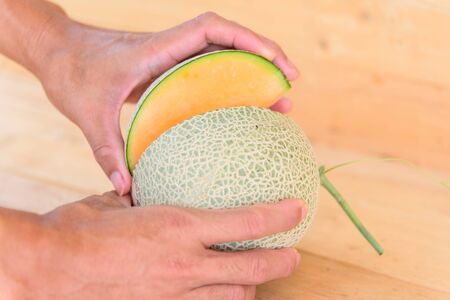The man use knife split the orange melon on wood plateの写真素材