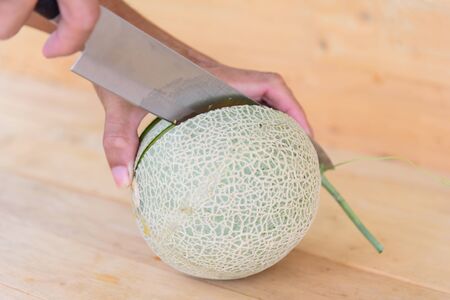 The man use knife split the orange melon on wood plateの写真素材
