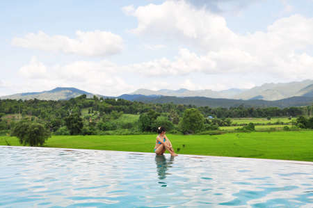 Woman sitting on edge of the swimming pool have beautiful Mountain scenery backgroundの写真素材