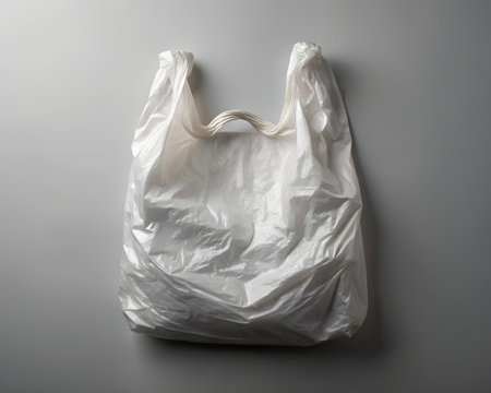 A white plastic shopping bag with twisted handles is presented from a topdown perspective on a neutral gray background, emphasizing its common utilityの素材