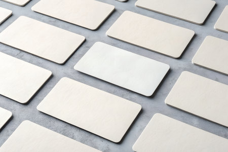 A collection of blank, lightcolored rectangular cards are arranged in a neat, organized pattern on a textured gray surface, suggesting a layout for business cards or notesの素材