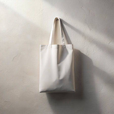 A plain beige canvas tote bag with white handles hangs on a textured beige wall, casting subtle shadowsの素材
